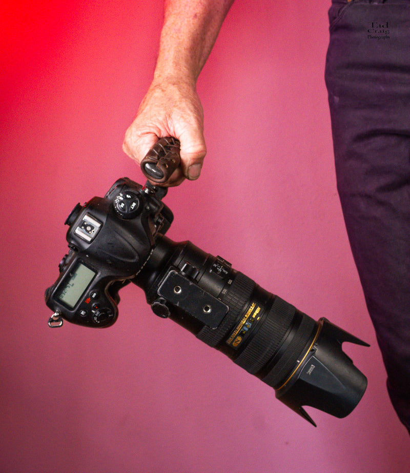 Hand Holding Camera Handle attached to a mirrorless camera with a large zoom lens attached